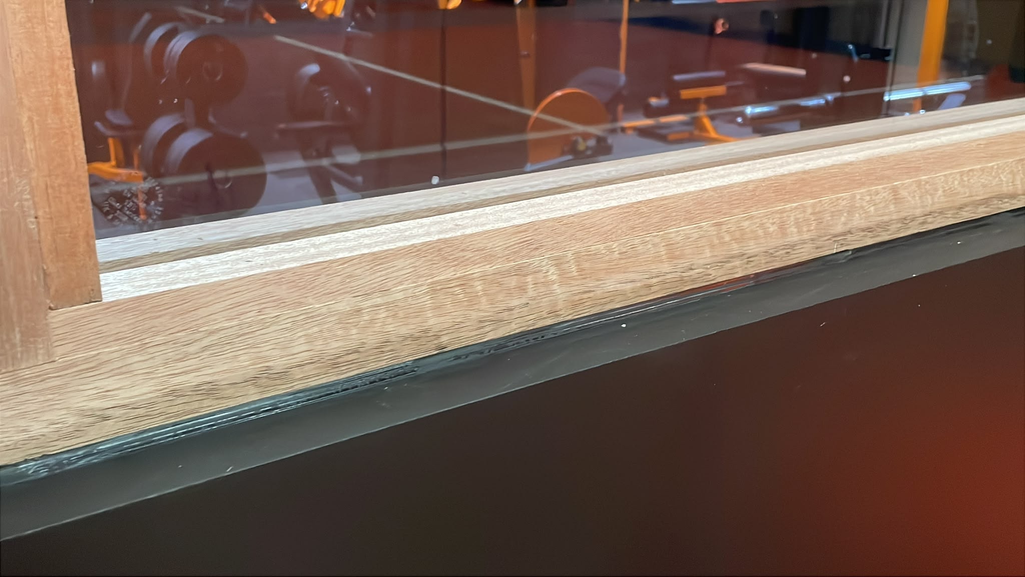 Close-up of silicone bead sealing oak window frame to dark wall